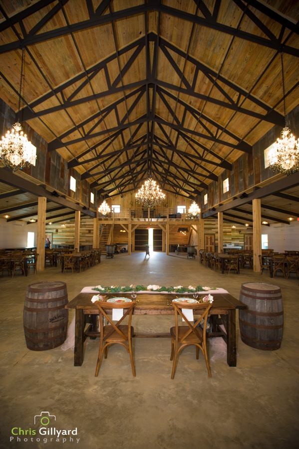barn interior with sweetheart table, barrels, beautiful chandeliers, and large wood beams
